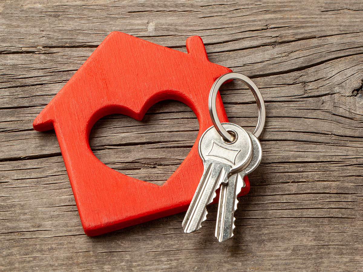 house keys with heart shaped house on wood background